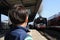 A young boy standing at the train station platform and looking at the locomotive train approaching