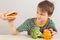 Young boy in a striped shirt at the table refuses hamburger in favor of healthy diet