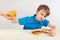 Young boy at the table chooses between fastfood and fruits on white background