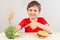 Young boy at the table chooses between hamburger and broccoli