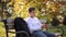 Young boy take out of his pocket smartphone. Teenage boy sitting on the bench in the park