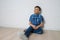 Young boy thinkin sitting near white white brick wall looking up, copy space available.