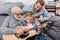 Young boy trying to learn playing guitar while his father and grandpa are