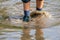 Young boy wading through mud of high tide with blue hiking shoes after a flood has broken the protecting dike