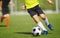 Young boy in yellow soccer jersey uniform running after ball on training pitch