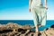 Young, brave woman standing on top of rock on a summer day watching epic sea landscape with dress moving in the wind , evocative