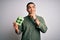 Young brazilian man holding carton box of healthy fresh eggs over white background serious face thinking about question, very