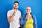 Young brazilian mother and son standing over blue background thinking concentrated about doubt with finger on chin and looking up