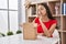 Young brazilian woman looking inside cardboard box thinking concentrated about doubt with finger on chin and looking up wondering