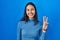 Young brazilian woman standing over blue isolated background showing and pointing up with fingers number three while smiling