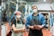 Young brewers in aprons and protective masks standing against large steel tanks