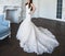 A young bride in a long stylish wedding dress stands in a chic room with a fireplace