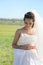 Young bride outdoor portrait in white dress against green field