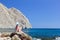 Young brunette beautiful woman sunbathing on rock on tropical beach.