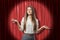 Young brunette business woman showing doubt with palms up on red stage curtains background