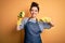 Young brunette cleaner woman wearing housekeeping gloves holding scourer scrub with surprise face pointing finger to himself