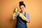 Young brunette cleaner woman wearing housekeeping gloves holding scourer scrub very happy pointing with hand and finger