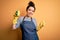 Young brunette cleaner woman wearing housekeeping gloves holding scourer scrub very happy pointing with hand and finger to the