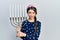 Young brunette girl holding menorah hanukkah jewish candle clueless and confused expression