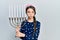 Young brunette girl holding menorah hanukkah jewish candle puffing cheeks with funny face