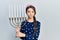 Young brunette girl holding menorah hanukkah jewish candle relaxed with serious expression on face