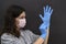 A young brunette girl puts on her left hand a blue medical disposable glove. Both hands in gloves. A woman wears a protective mask