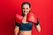 Young brunette girl using boxing gloves sticking tongue out happy with funny expression