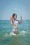 Young brunette girl in white bikini and wet t-shirt playing in the water