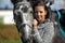 Young brunette with gray horse in a field in summer