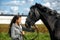 Young brunette with gray horse in a field in summer