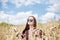 Young brunette hippie woman, wearing boho style clothes, sitting in the middle of wheat field with blue sky, meditating, thinking