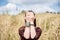 Young brunette hippie woman, wearing boho style clothes, sitting in the middle of wheat field with blue sky, meditating, thinking