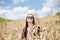 Young brunette hippie woman, wearing boho style clothes, sitting in the middle of wheat field with blue sky, meditating, thinking