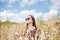 Young brunette hippie woman, wearing boho style clothes, sitting in the middle of wheat field with blue sky, meditating, thinking