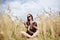 Young brunette hippie woman, wearing boho style clothes, sitting in the middle of wheat field with blue sky, meditating, thinking