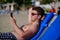 A young brunette man in sunglasses sunbathes on the sea coast, lies on a lounger and takes a selfie using a smartphone