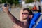 A young brunette man in sunglasses sunbathes on the sea coast, lies on a lounger and takes a selfie using a smartphone