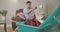 Young brunette man throwing laundry into basket as sitting on armchair at the background. Caucasian male housekeeper