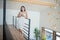 Young brunette in night dress standing on the top of stairs, holding white cup, leaning on stair rails