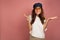 Young brunette in a white t-shirt throws up her hands as if she says `oops`, pink background