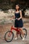 A young brunette woman of Asian appearance in a dark blue dress is standing next to a bicycle with a punctured wheel. there is a