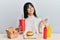 Young brunette woman with bangs eating a tasty classic burger with ketchup and mustard celebrating achievement with happy smile