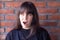 Young brunette woman with bangs wearing a black t-shirt shock by an unpleasant surprise on brick wall background