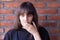 Young brunette woman with bangs wearing a black t-shirt shock by an unpleasant surprise on brick wall background