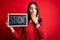 Young brunette woman with blue eyes holding blackboard with strong word message cover mouth with hand shocked with shame for