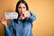 Young brunette woman with blue eyes holding paper with you are fired message pointing with finger to the camera and to you, hand