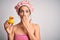 Young brunette woman with blue eyes wearing bath towel and shower cap holding duck toy cover mouth with hand shocked with shame