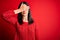 Young brunette woman with blue eyes wearing casual sweater over isolated red background covering eyes with hand, looking serious