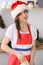 Young brunette woman cooking pizza or handmade pasta while wearing Santa Claus cap in the kitchen. Housewife preparing