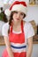 Young brunette woman cooking pizza or handmade pasta while wearing Santa Claus cap in the kitchen. Housewife preparing